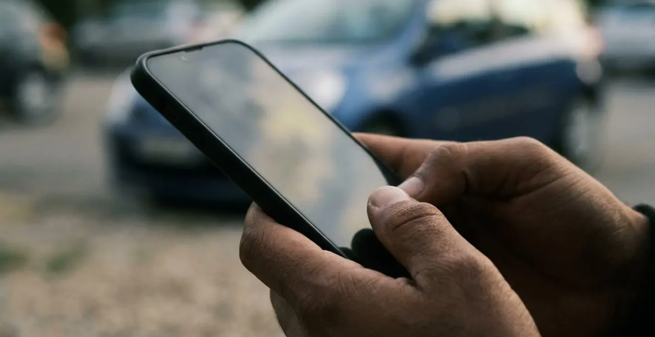 Main tenant un smartphone montrant un écran flou avec une voiture française en arrière-plan, symbolisant la consultation dématérialisée du FVA.